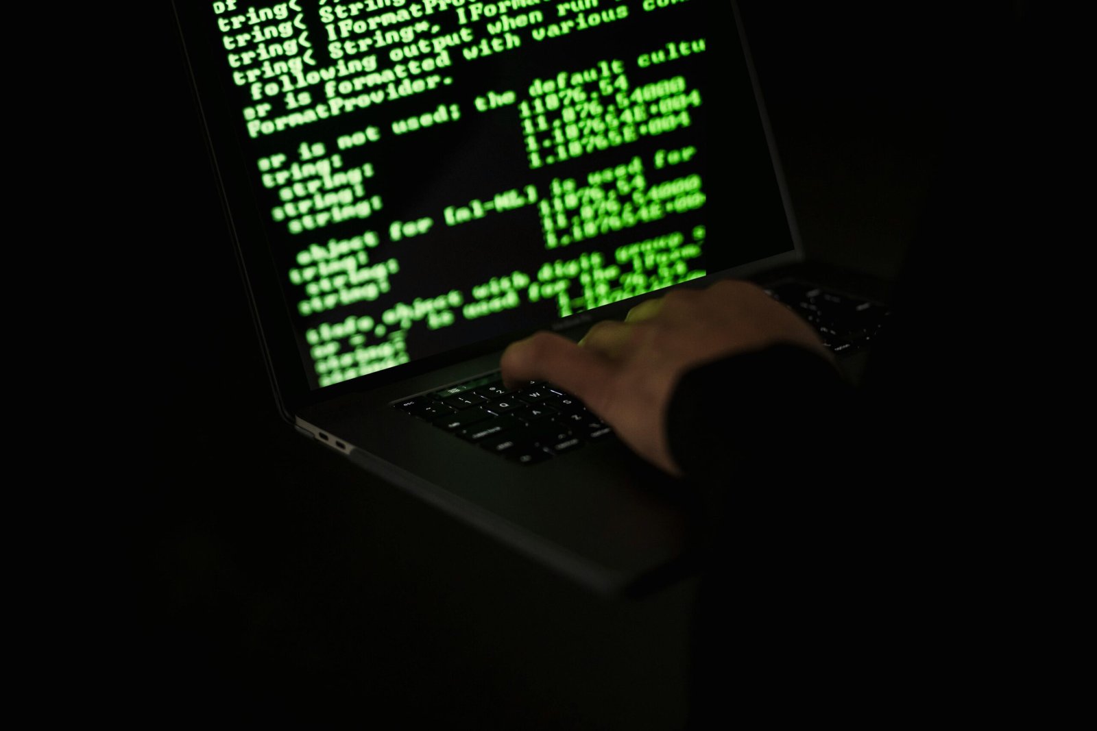 Home Silhouette of a hacker typing on a laptop in the dark with green code on screen.
